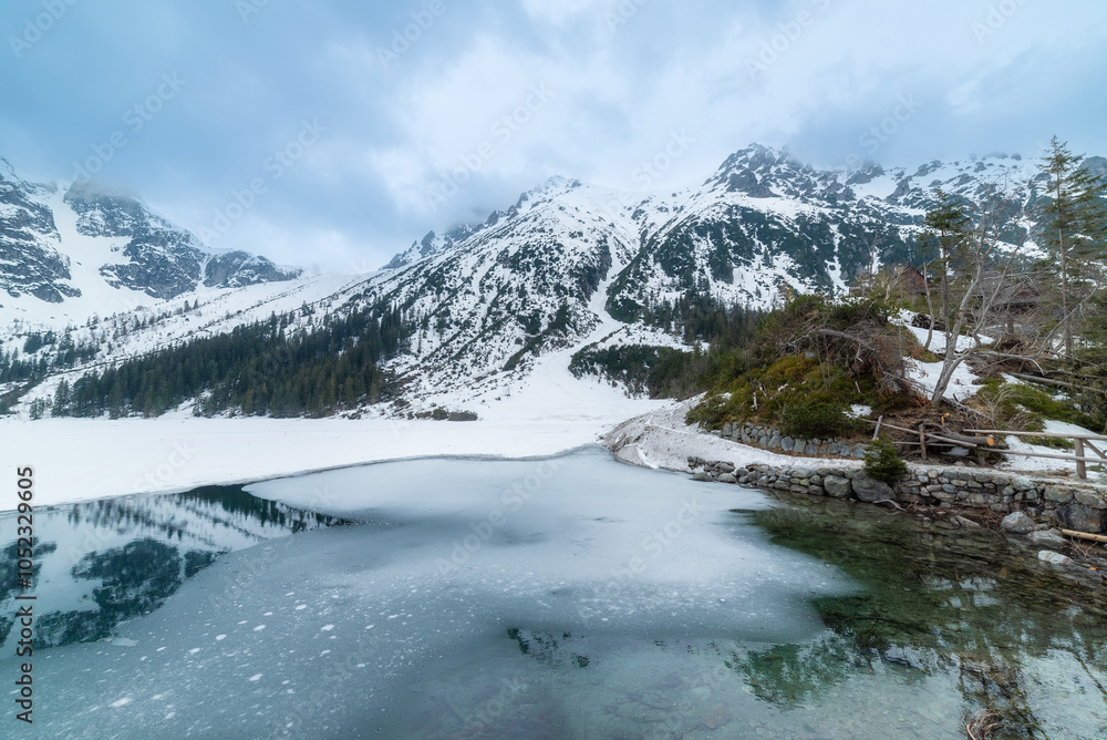 Obraz premium tranquil view of Morskie Oko in Tatra National Park, Poland, showcasing majestic snow-covered mountains, serene frozen lake, and reflections on a chilly winter day. Winter landscape