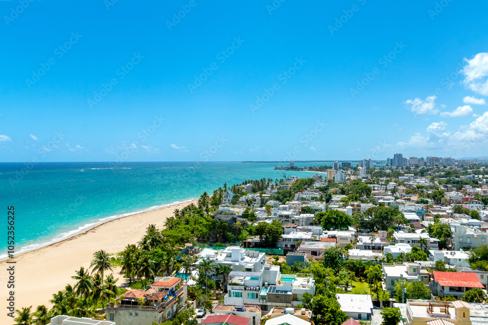 Obraz premium Aerial view of the residential community of Ocean Park in San Juan, Puerto Rico. Showcasing the wide sandy beaches, turquoise ocean, and filled with a tropical city skyline in the background.