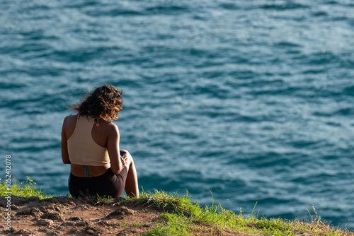 Rear view of a young woman enjoying the awesome sea view, sitting on the top of mountain during summer vacation photo