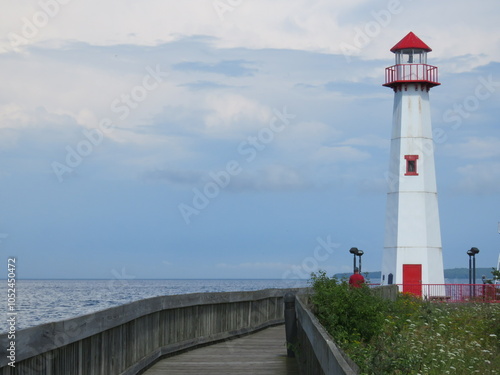 Tall White St Ignace Michigan Lighthouse with Red Roof Window and Door Down Boardwalk on Coast of Lake Huron under Beautiful Clouds and Sky photo