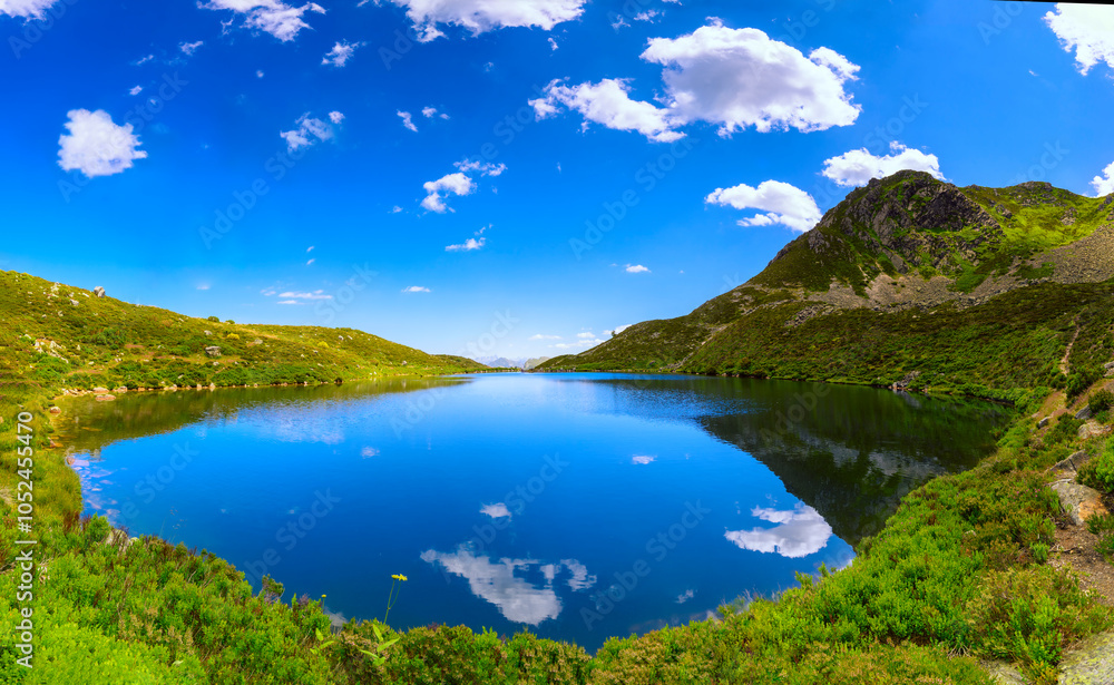 Naklejka premium Panoramic view of a mountain lake. The blue sky with clouds reflecting on the mirrored lake water