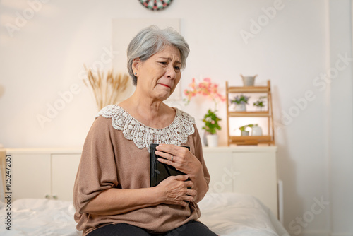 An elderly Asian woman with short white hair is thinking of her loved one, hugging a picture of the person she is missing and crying.