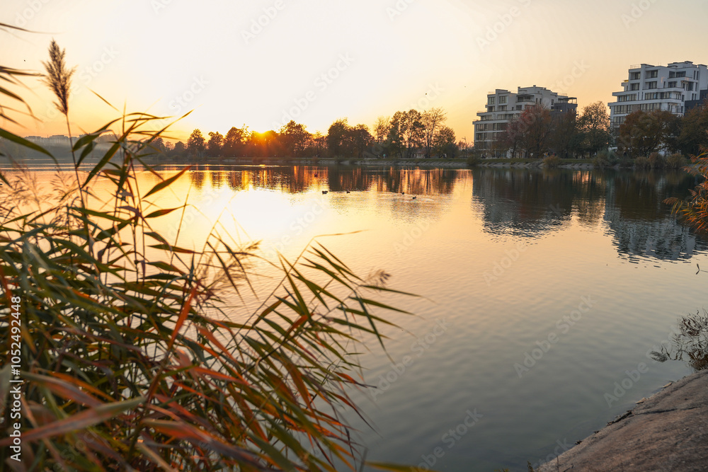 Obraz premium Romantic sunset on a lake. The sun is barely visible because of the silhouettes of the trees. Dawn on the lake, the sun comes out of the trees. autumn landscape in the evening.