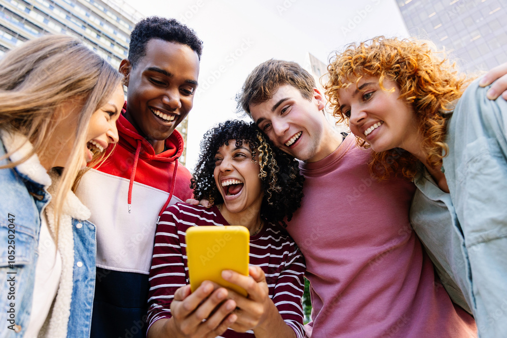 Happy young group of diverse teenage friends using mobile phone at city street. Generation Z people having fun watching media content on social platform app outside. Youth community concept