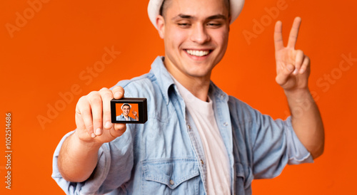Happy handsome guy tourist posing and using action camera over orange studio background