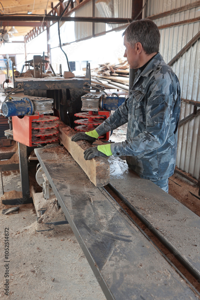 A worker saws a tree trunk on a machine. The sawmill. The process of processing logs at a sawmill. The concept of production. Vertical photo. A worker saws a tree trunk on a machine. The sawmill. The process of processing logs at a sawmill. The concept of production. Vertical photo.