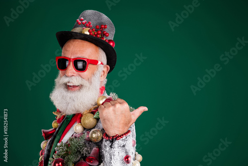 Photo of funny elderly white hair santa man point empty space wear balls baubles on jacket hat isolated on green color background