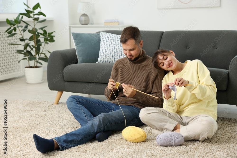 Woman teaching her boyfriend how to knit on floor at home Woman teaching her boyfriend how to knit on floor at home