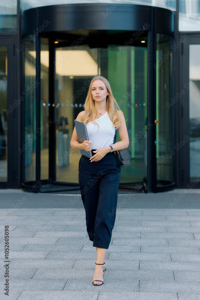 Fototapeta premium Career concept, young blonde woman in white t-shirt with laptop in hands leaving office
