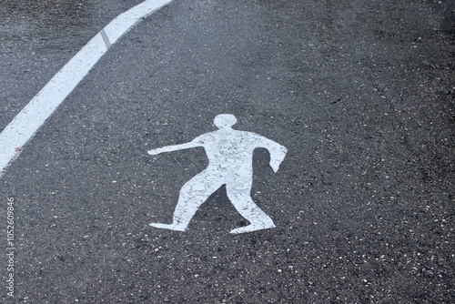 Pedestrian Symbol on Wet Asphalt Road: Street Crossing Marking Reflecting in Rainy Weather, Emphasizing Urban Safety, Traffic Direction, and Caution