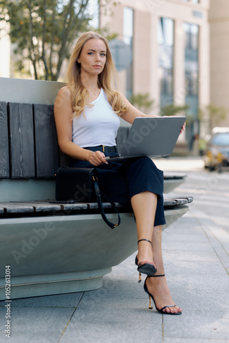 European young business woman wastes no time and checks work chats on laptop on street