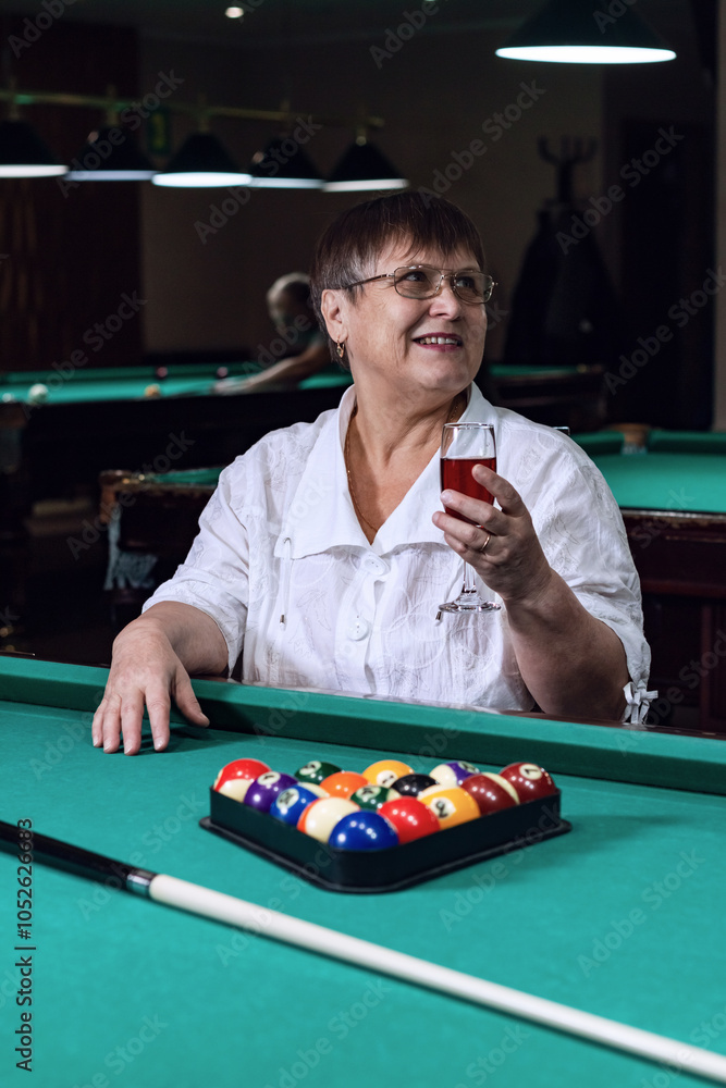 An elderly woman relaxes in a billiard club, drinking wine. An elderly woman relaxes in a billiard club, drinking wine.