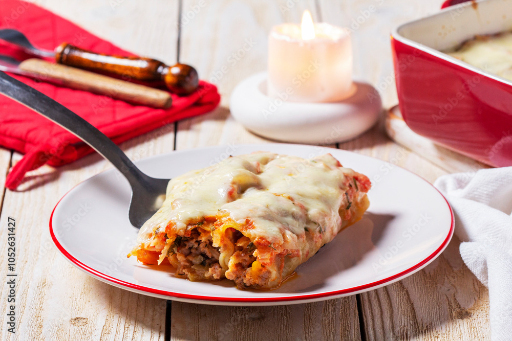 Cannellone with meat filling, tomato sauce and cheese on a light wooden table.
