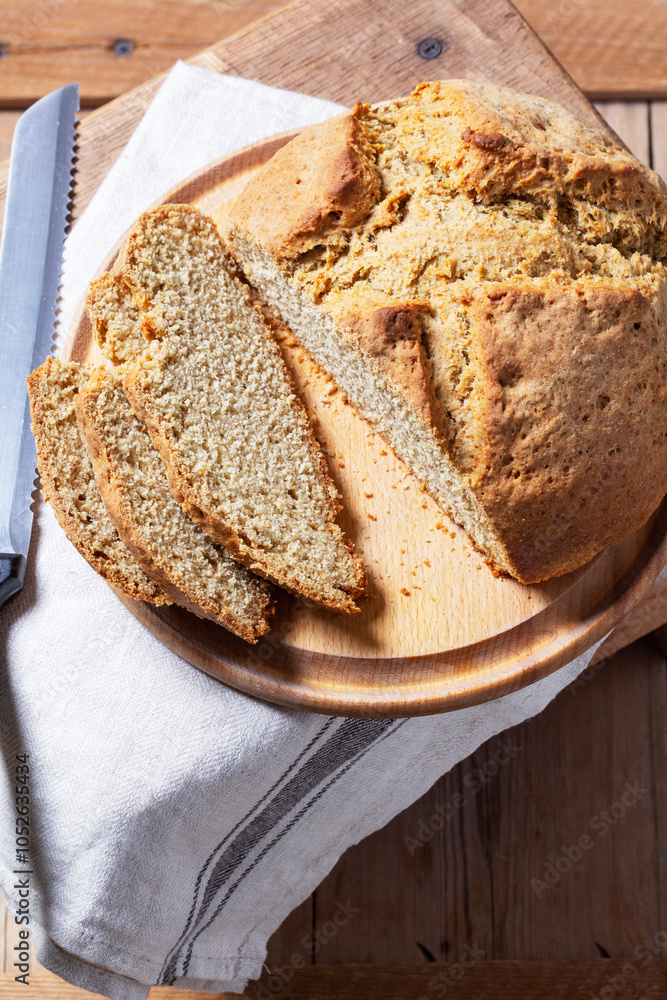 Homemade Irish soda bread cut into pieces and knife on wooden background.