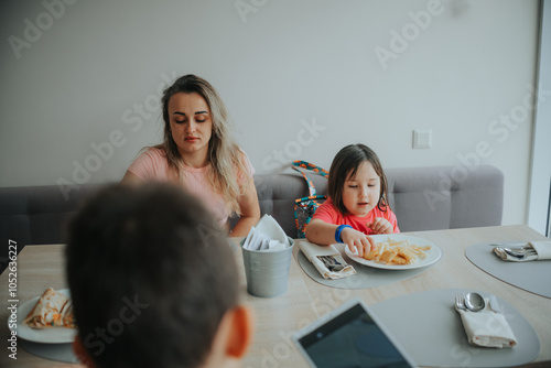 A woman and a child are eating at a table with a laptop in front of them photo