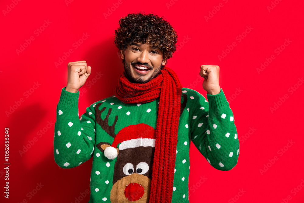 Photo of nice young man raise fists wear christmas sweater isolated on red color background Photo of nice young man raise fists wear christmas sweater isolated on red color background