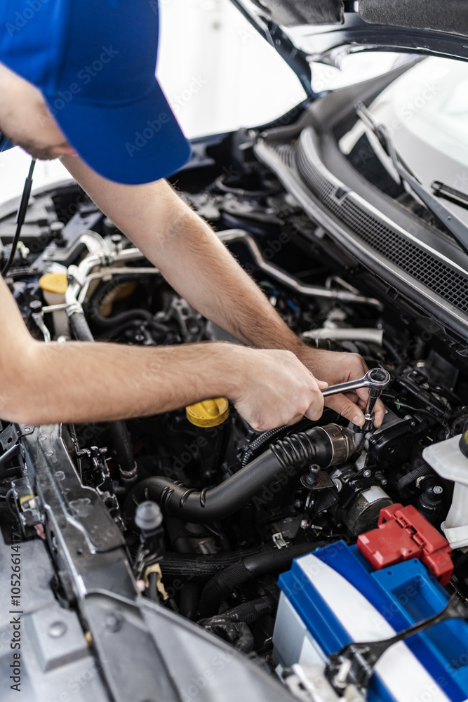A mechanic repairs an engine with tools inside a vehicle at an auto shop during daylight hours, showcasing hands-on automotive work A mechanic repairs an engine with tools inside a vehicle at an auto shop during daylight hours, showcasing hands-on automotive work