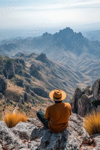 Hiker resting on a rock while overlooking a vast mountain landscape at sunrise