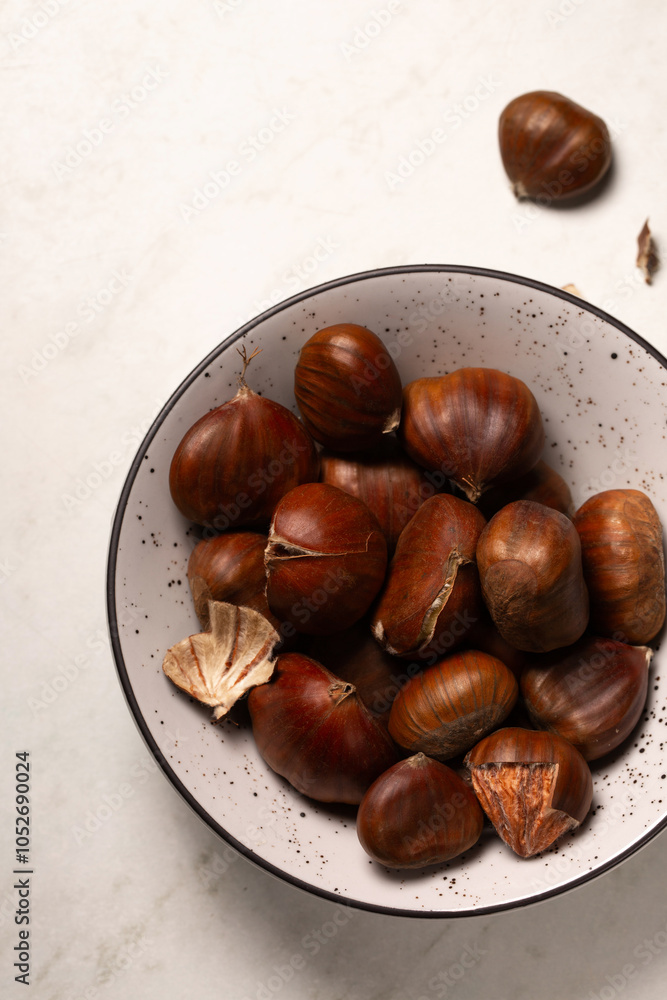 Delicious edible chestnuts in a small bowl on a white table Delicious edible chestnuts in a small bowl on a white table