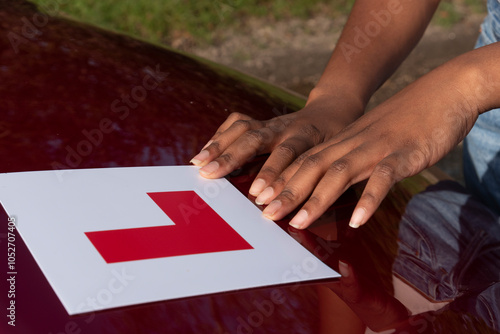 Hampshire England UK. 27.10.2024. Learner driver attaching L plate to bonnet of a red car.