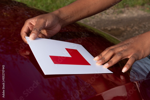Hampshire England UK. 27.10.2024. Learner driver attaching L plate to bonnet of a red car.