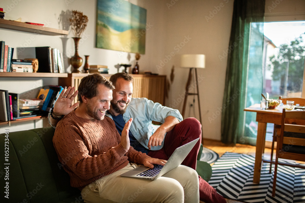 Gay male couple having video call with laptop on couch at home Gay male couple having video call with laptop on couch at home