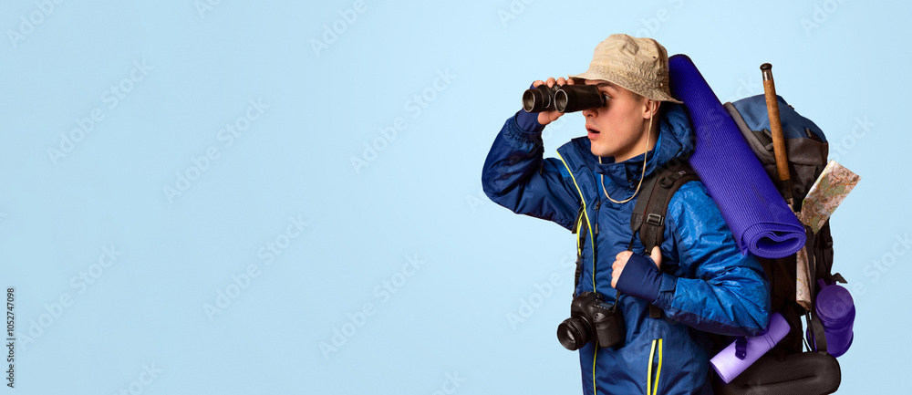 Backpacker looking through binoculars at free space, orange studio background Backpacker looking through binoculars at free space, orange studio background