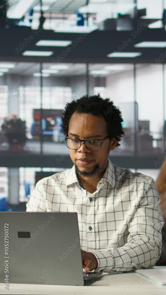 Vertical video Account executive multitasking on his computer to finish business tasks and operations. African american man reviewing financial documents for company success, productivity. Camera B. Vertical video Account executive multitasking on his computer to finish business tasks and operations. African american man reviewing financial documents for company success, productivity. Camera B.