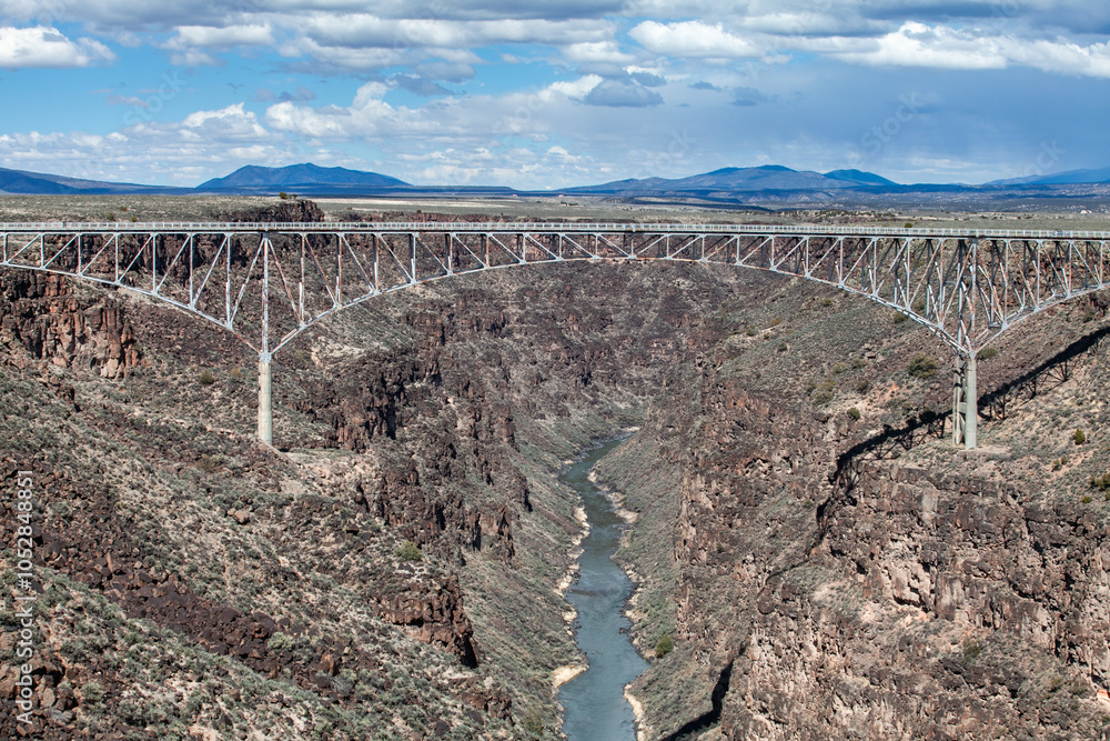 Fototapeta premium Rio Grande Gorge Bridge near Santa Fe, New Mexico, this steel arch bridge spans a deep canyon carved by the Rio Grande River, showcasing a stunning example of engineering amidst a rugged, high desert