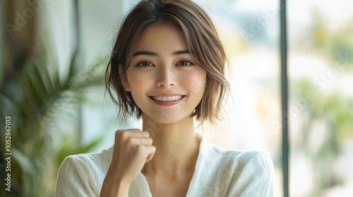 A photo of an Asian woman with short hair, smiling and clenching her fist in victory on a white background