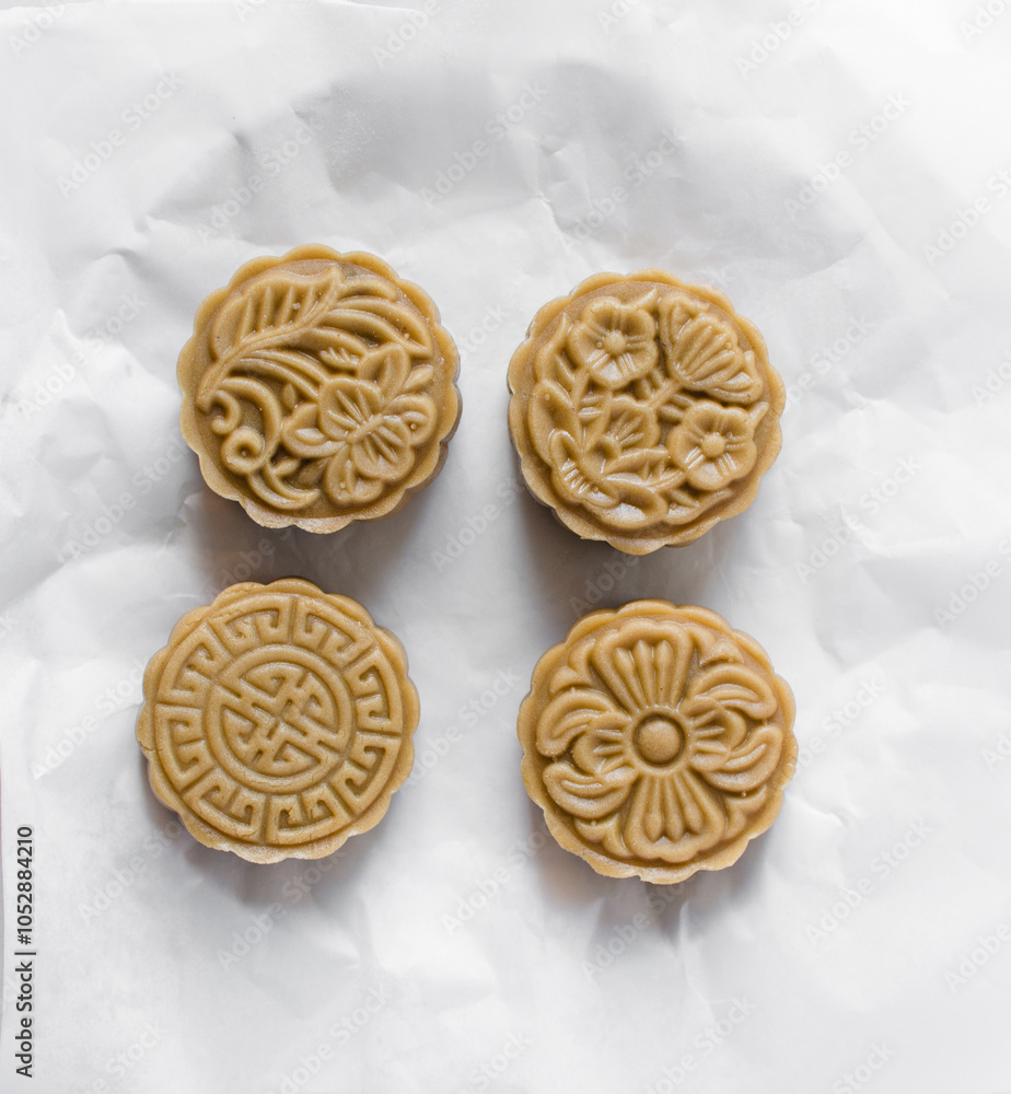 Overhead view of homemade mooncakes, top view of raw mooncakes on white parchment paper, process of making mooncakes for Lunar New Year Overhead view of homemade mooncakes, top view of raw mooncakes on white parchment paper, process of making mooncakes for Lunar New Year