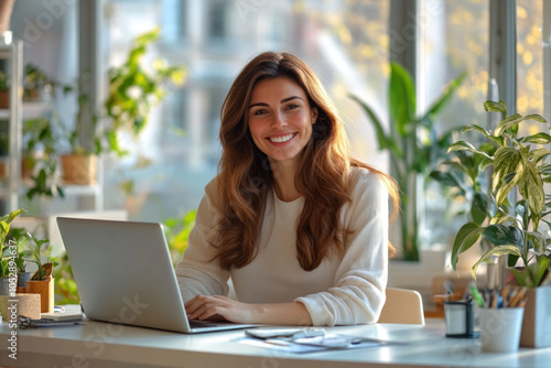 Woman sitting at desk with laptop, focused expression, typing intensively. Bright workspace, plants in background, natural light pouring in through window.