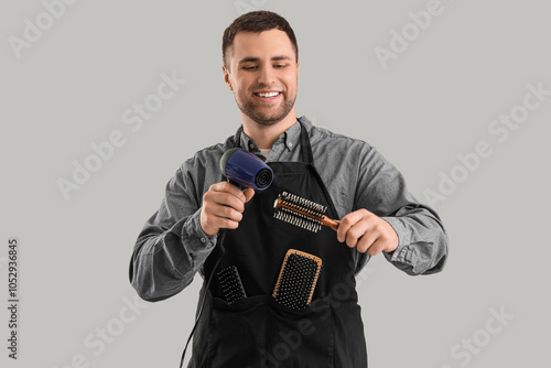 Male hairdresser with dryer and brush on light background