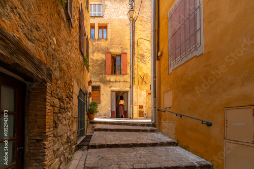 A young woman stands in the doorway near a narrow cobblestone alley in the medieval hilltop village of Tourrettes-sur-Loop, France, in the Alpes-Maritimes region. photo