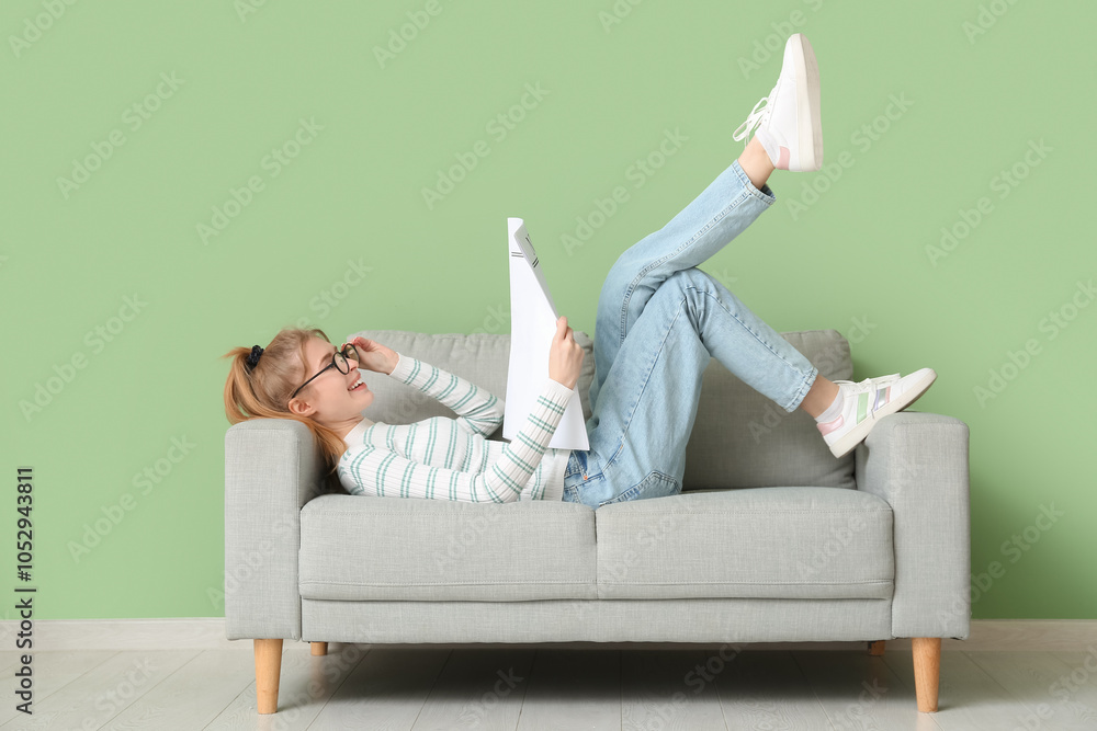 Obraz premium Young woman reading newspaper while lying on sofa near green wall