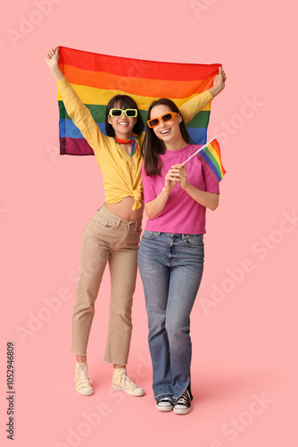 Young lesbian couple in sunglasses with LGBT flags on pink background