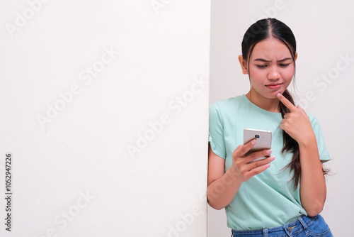 A woman leaning on the wall showing confused face when staring at her phone photo