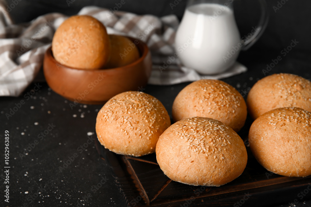 Wooden board and bowl of fresh buns with sesame seeds on black background Wooden board and bowl of fresh buns with sesame seeds on black background
