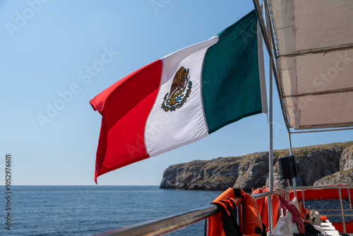 Mexican flag flying in the foreground. Out of focus in the background Marietas Island - conservation area in Puerto Vallarta, Jalisco,. Blue sky, sunny day. Travel and tourism concept. photo