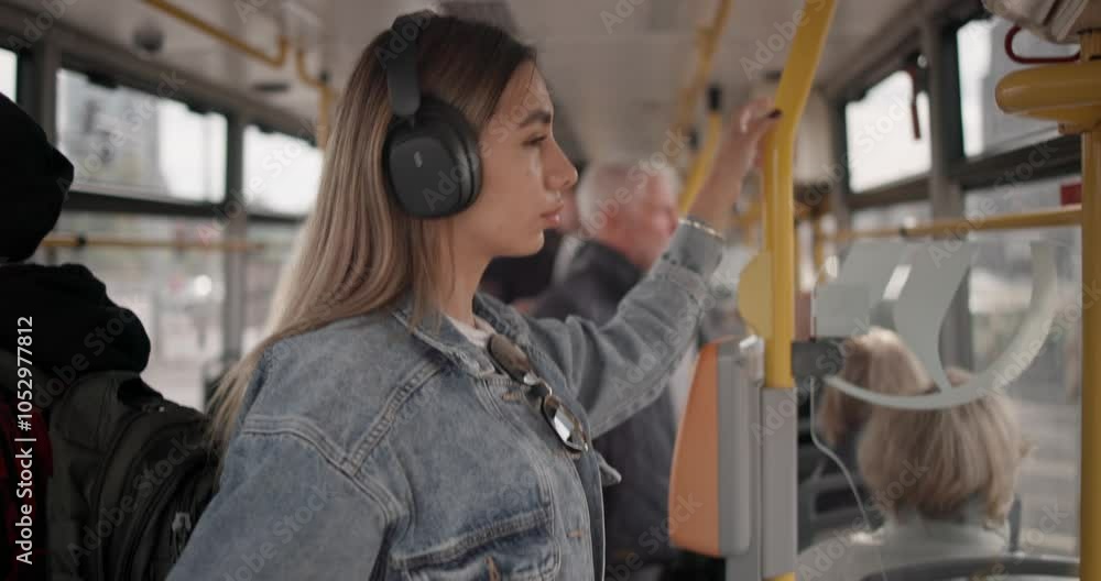 Handheld video of a young girl in a casual denim jacket riding a city tram and putting on wireless headphones to listen to music from her phone Handheld video of a young girl in a casual denim jacket riding a city tram and putting on wireless headphones to listen to music from her phone