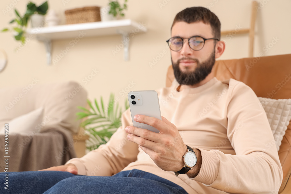Young bearded man working with mobile phone in armchair at home, closeup Young bearded man working with mobile phone in armchair at home, closeup