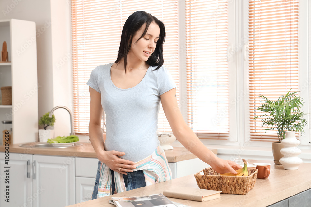 Young pregnant woman taking banana from basket in kitchen Young pregnant woman taking banana from basket in kitchen