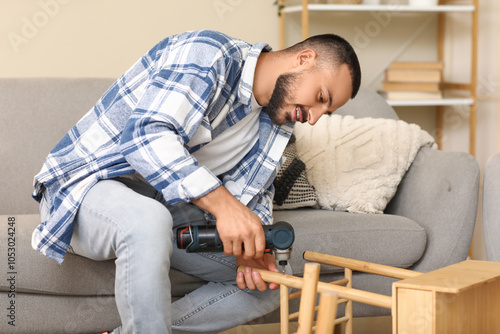 Young man with drill assembling wooden table at home