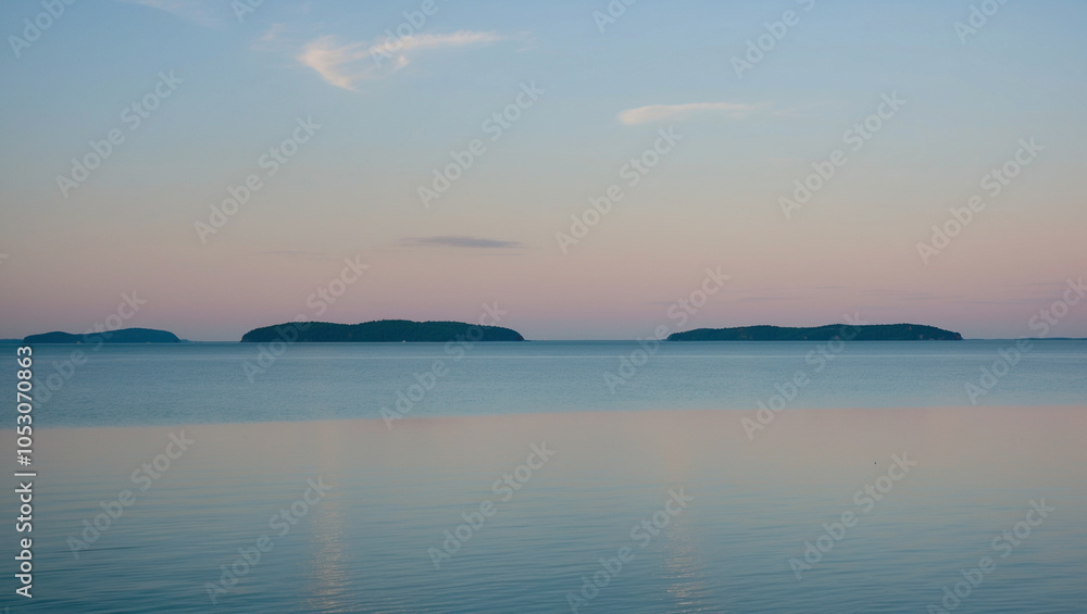 Obraz premium Tranquil Lake Under a Pastel Morning Sky with Distant Islands on the Horizon