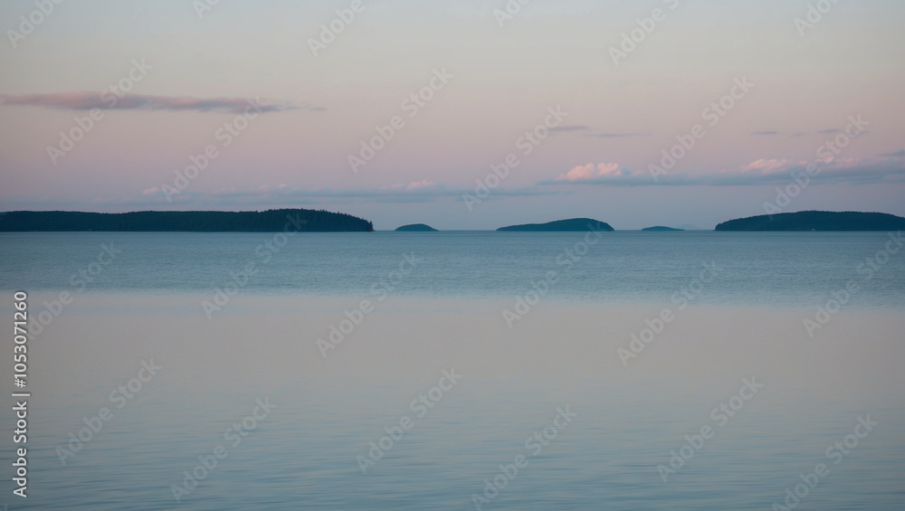 Obraz premium Tranquil Lake Under a Pastel Morning Sky with Distant Islands on the Horizon