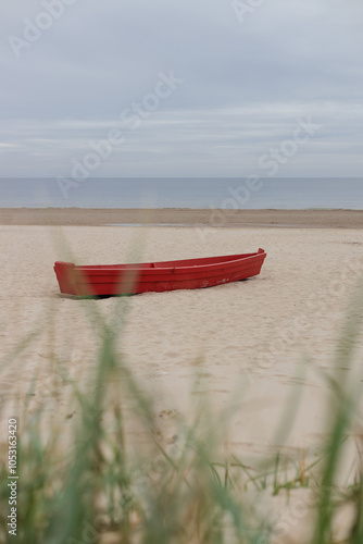 Red boat on a sandy beach against moody sky photo