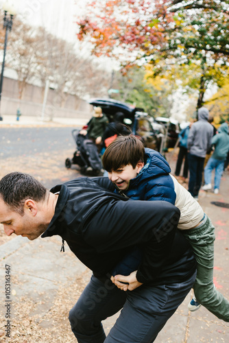 Dad gives son piggyback ride in urban area with fall leaves