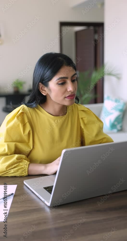 Serious busy young Indian freelancer girl working from home, typing on laptop at workplace table, watching, reading online content, using Internet communication for distant job, education