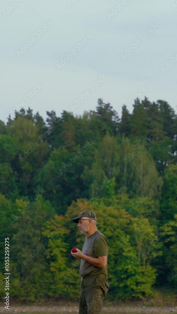 Vertical video of senior men taking a bite into a red apple. Eating outdoors with verdant forest in the background. Vertical video of senior men taking a bite into a red apple. Eating outdoors with verdant forest in the background.