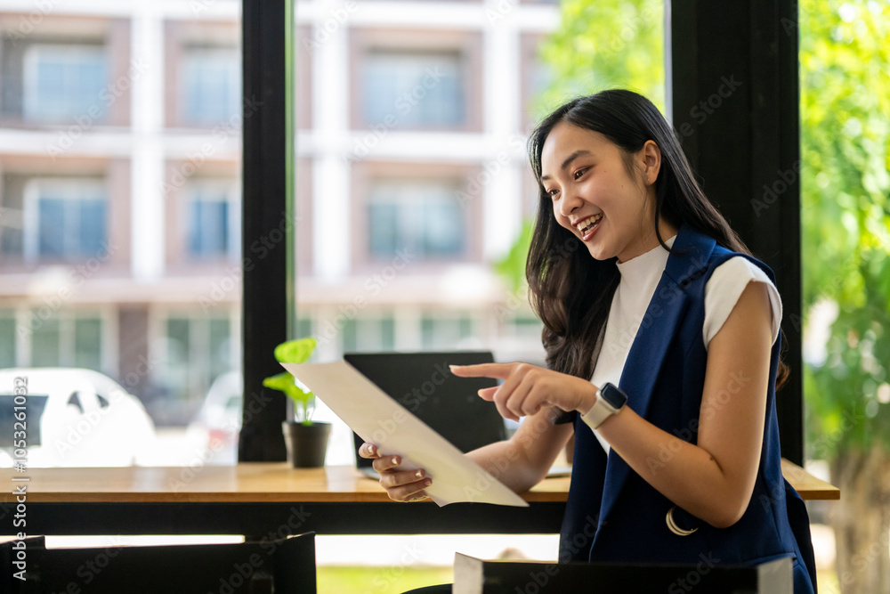 A woman is sitting at a table with a laptop and pointing to a piece of paper A woman is sitting at a table with a laptop and pointing to a piece of paper